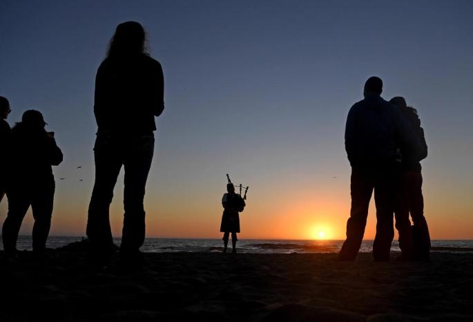 Bagpiper Elise MacGregor Ferrell plays funeral music at sunset, for a beachside ceremony at Moss Landing, California.